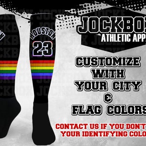 May include: A pair of black athletic socks with a rainbow stripe design. The socks feature the text "HOUSTON" and the number "23" in white. The text "JOCKBOX ATHLETIC APPAREL" is displayed above the socks. The text "CUSTOMIZE WITH YOUR CITY & FLAG COLORS" is displayed below the socks. The text "CONTACT US IF YOU DON'T SEE YOUR IDENTIFYING COLORS" is displayed at the bottom of the image.
