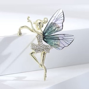 May include: A gold-toned fairy brooch with iridescent wings and a sparkling crystal dress. The wings are a mix of green and purple.