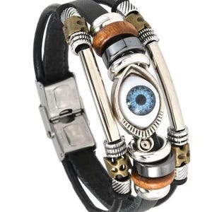 May include: Black leather bracelet with silver-tone metal accents, wooden beads, and an eye-shaped charm with a blue iris. The bracelet features a stainless steel clasp and a multi-strand design.