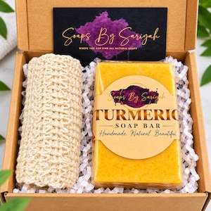 Puede incluir: Una caja de regalo de cartón que contiene una pastilla de jabón de cúrcuma amarilla rectangular envuelta en plástico transparente con la etiqueta Soaps By Sariyah Turmeric Soap Bar Handmade. Natural. Beautiful. y un paño beige.