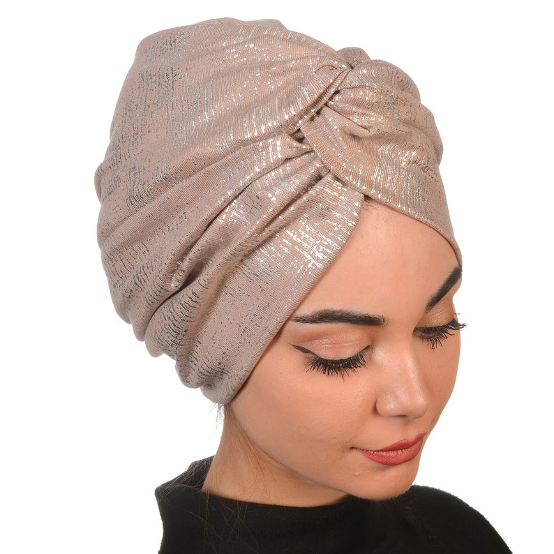 May include: A light brown turban with a shimmery silver metallic finish. The turban is made of a soft, stretchy fabric and is designed to be worn as a head covering.