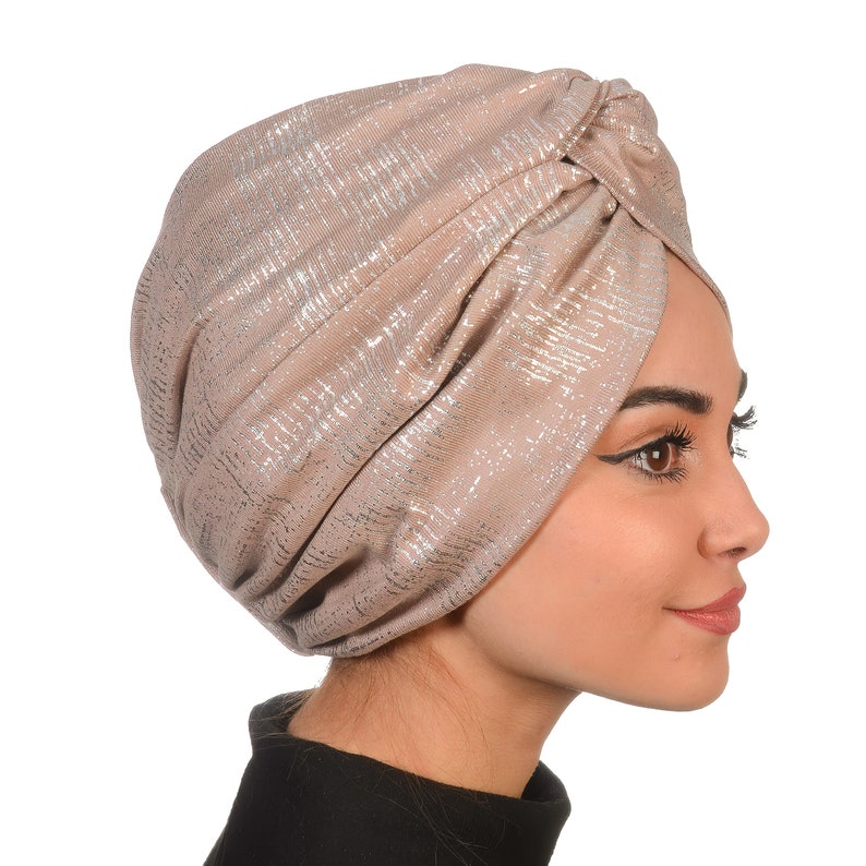 May include: A beige turban with a silver shimmer pattern. The turban is made of a soft, stretchy fabric and is designed to be worn as a head covering.