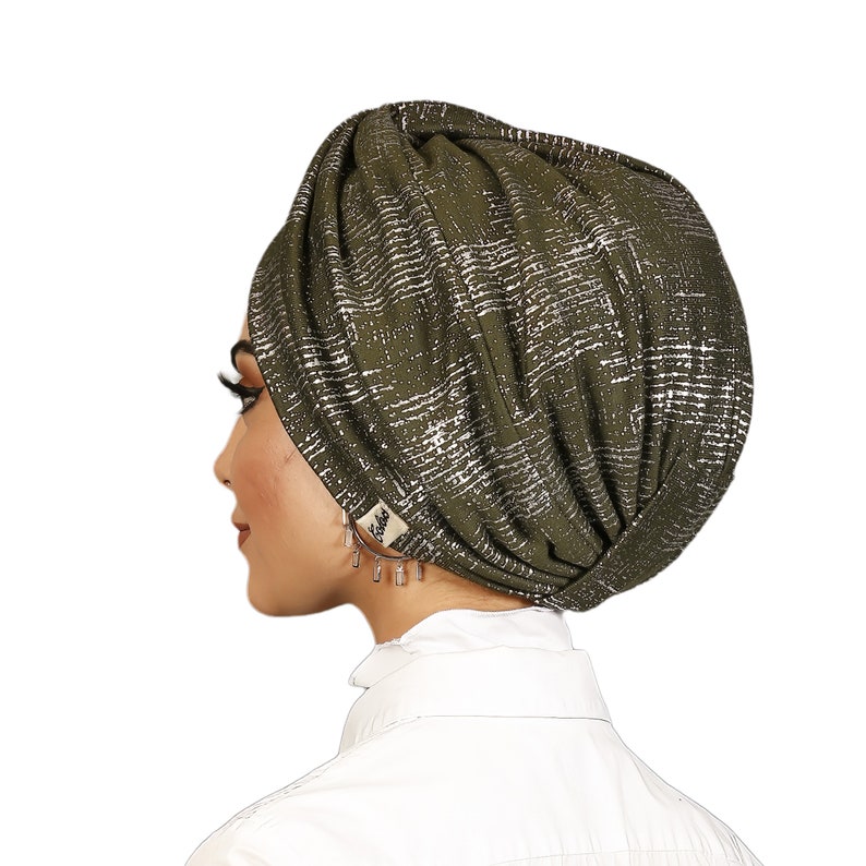 May include: A green turban with a silver metallic pattern. The turban is made of a soft, stretchy fabric and is designed to be worn as a headscarf.