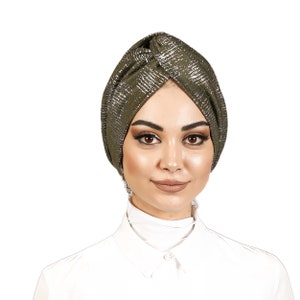 May include: A green turban with silver glitter accents. The turban is styled with a knot on top and is worn by a person with a white shirt.