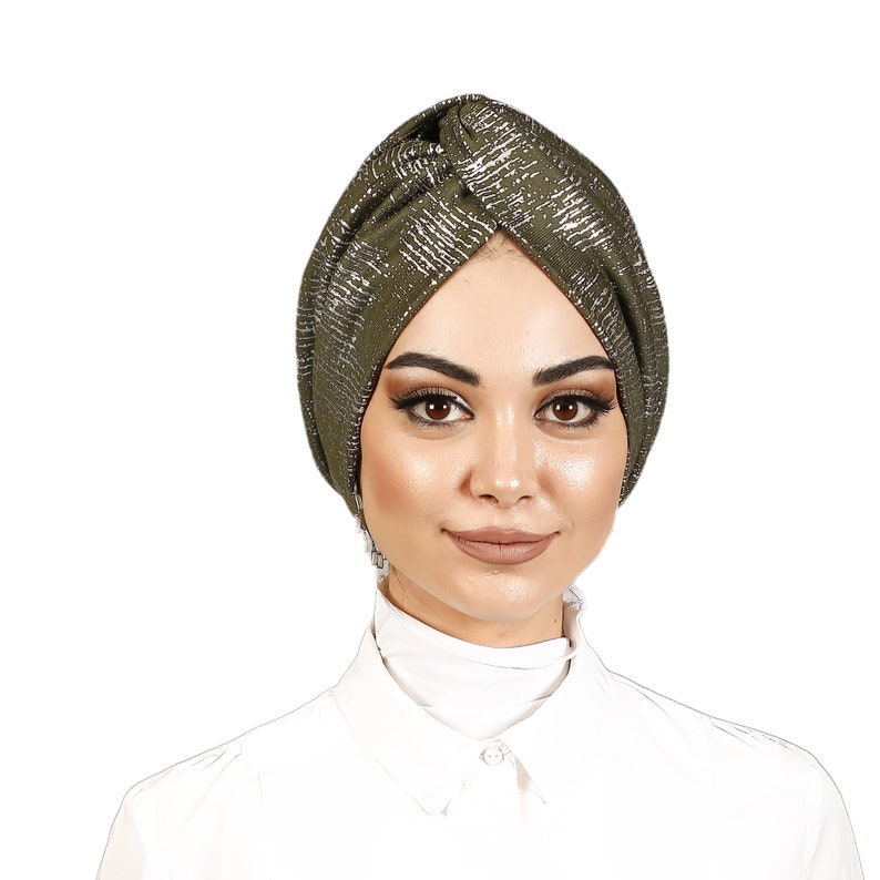 May include: A green turban with silver glitter accents. The turban is styled with a knot on top and is worn by a person with a white shirt.