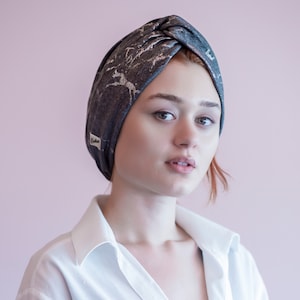 May include: A woman wearing a gray and silver turban with a white label that says "Godiva". She is wearing a white button-down shirt.
