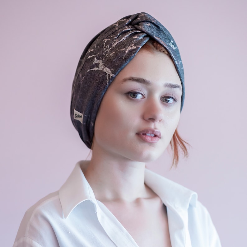 May include: A woman wearing a gray and silver turban with a white label that says "Godiva". She is wearing a white button-down shirt.