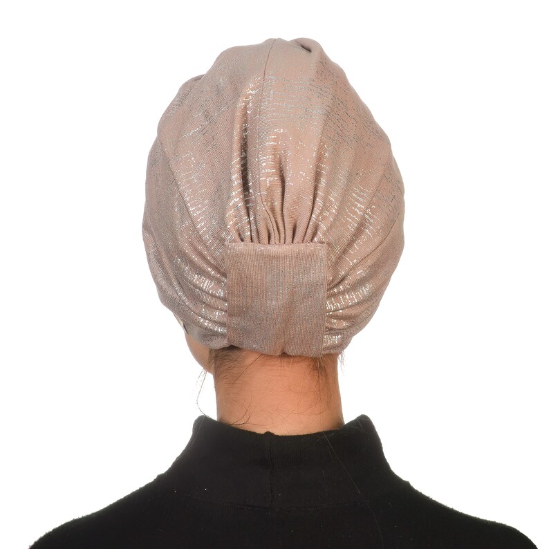 May include: A light brown turban with silver shimmer, worn on a person's head. The turban is made of a soft, stretchy fabric.