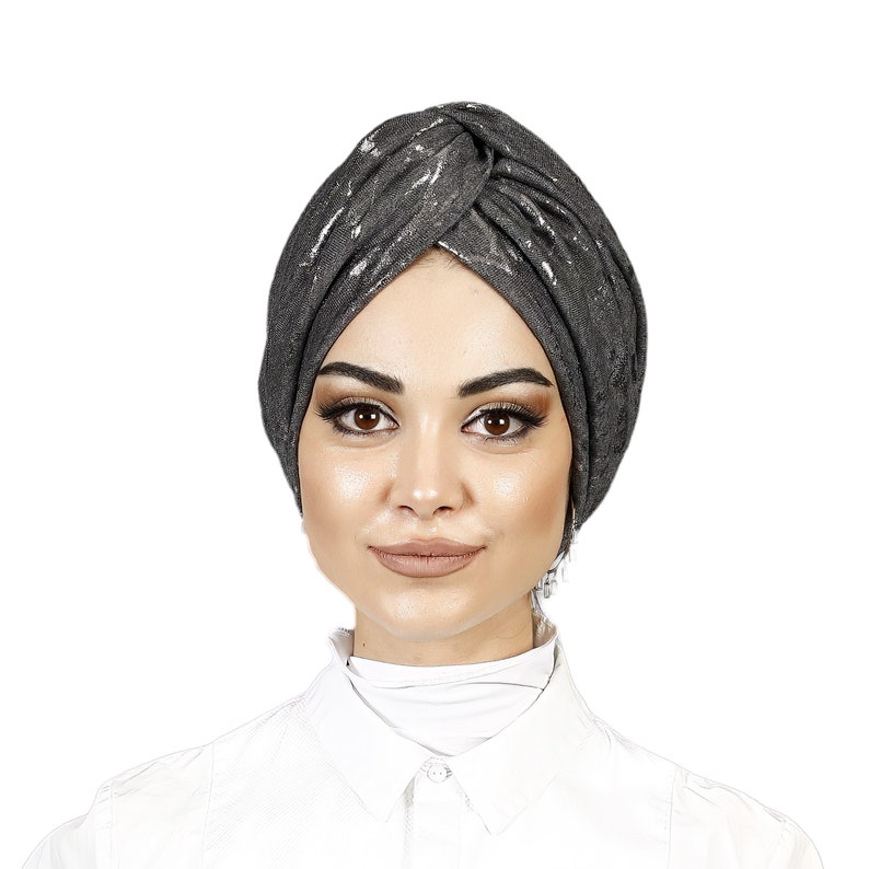May include: A woman wearing a gray turban with silver accents. The turban is tied in a knot on top of her head. She is wearing a white collared shirt.