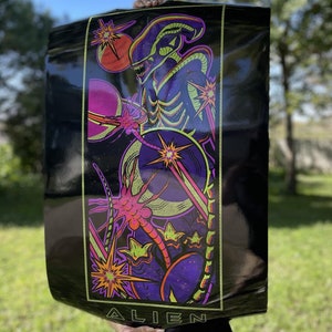 May include: A black poster with a neon green and purple alien creature with a large head and long tail. The alien is surrounded by stars and planets. The poster has the word "ALIEN" printed at the bottom.