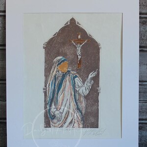 May include: Artwork print of a religious figure with a gold halo, wearing a white and blue robe, and a brown background. The print is in a white mat. A candle and a book are in the foreground. Text on the image: "Please message me for images of additional color artwork available, as colors vary from peice to peice."