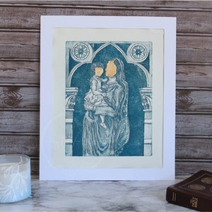 May include: A blue and white print of a mother and child in an arched doorway. The print is framed in white.