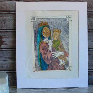 May include: A framed print depicting a religious scene. The artwork features a woman in a red robe and blue veil holding a child. Both figures wear gold crowns and have gold-colored faces. The print is set against a textured background.