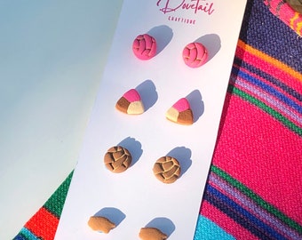 May include: A set of six colorful polymer clay earrings featuring Mexican sweet bread designs. The earrings are displayed on a white card with the text "Dovetail Craftique".