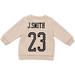 May include: A beige long-sleeve sweatshirt featuring the text J.SMITH in black capital letters above the number 23 in a large black athletic font. The garment has a crew neckline and ribbed cuffs at the sleeves and hem, providing a clean look.