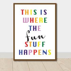 Puede incluir: Una impresión enmarcada con el texto "This is where the fun stuff happens" en colores arcoíris. Las palabras "fun stuff" están en cursiva negra.