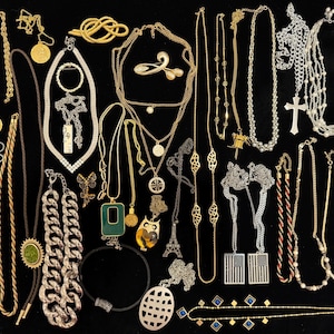 Op de afbeelding: Een verzameling kettingen in verschillende stijlen en materialen, waaronder goud, zilver en kralenontwerpen. De collectie bevat hangers, kettingen en statement-stukken, met een verscheidenheid aan lengtes en texturen. De kettingen worden op een zwart oppervlak weergegeven.