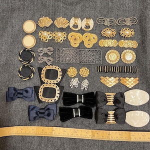 May include: A selection of vintage jewellery components, including gold-toned clasps, bow-shaped embellishments, and earrings. The assortment features various shapes and textures, such as round, seashell, and bow designs. Some pieces have pearl or rhinestone accents.