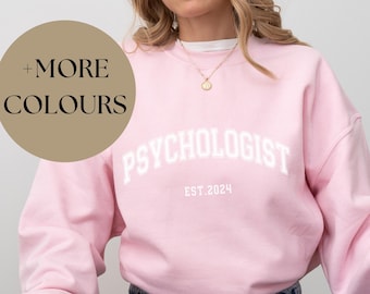 May include: A pink sweatshirt with the text "PSYCHOLOGIST EST. 2024" in white.
