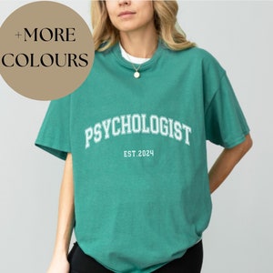 Könnte beinhalten: Ein türkisfarbenes T-Shirt mit dem Text "Psychologist Est. 2024" in weißen Buchstaben. Das Shirt ist Oversize und hat eine lockere Passform.