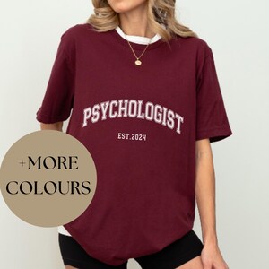 May include: Burgundy t-shirt with the text "Psychologist Est. 2024" in white. The t-shirt is oversized and has a relaxed fit.