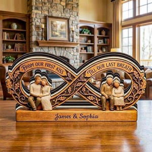 May include: A wooden infinity symbol sculpture with the text "From Our First Kiss" and "Till Our Last Breath." It features carved figures of couples and the names "James & Sophia." The sculpture is brown, black, and cream-colored.