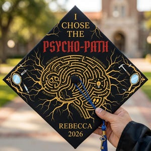 Op de afbeelding: Zwarte afstudeerhoed met gouden en rode tekst met de tekst "I Chose The Psycho-Path". De hoed heeft een hersen-doolhofontwerp met de woorden "Profiling" en "Criminology". De naam "Rebecca" en het jaar "2026" worden ook weergegeven.