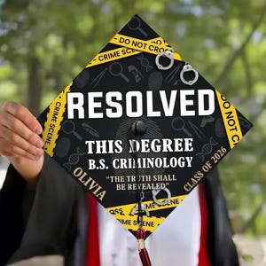 Op de afbeelding: Een zwarte afstudeerhoed met het woord "RESOLVED" in het wit. De hoed heeft elementen van een plaats delict, waaronder handboeien, vingerafdrukken en de tekst "THIS DEGREE B.S. CRIMINOLOGY". De naam "OLIVIA" is ook zichtbaar.
