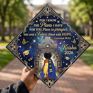 以下が含まれることがあります： 卒業式の帽子。紺色で、金色の装飾とエレガントなデザインが施されています。聖書の一節、蝶、卒業のシンボル、名前「Keisha」、年号「2026」が特徴です。テーマは天体です。