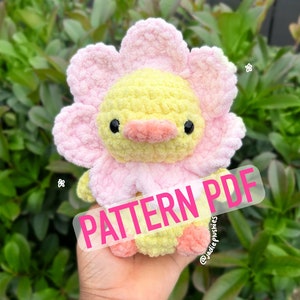 May include: A crochet pattern for a yellow and pink flower-shaped plush toy. The pattern is available as a PDF download. The text "PATTERN PDF" is written in pink letters on a white background.