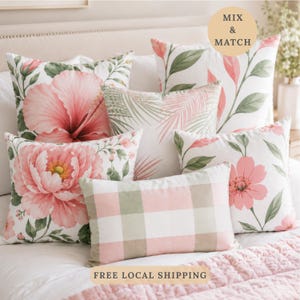 May include: A collection of square and rectangular throw pillows featuring various botanical prints with pink flowers, green leaves, and a pink and white gingham pattern. The pillows are arranged on a bed with a white quilted coverlet.