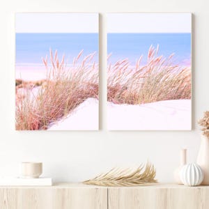 Könnte beinhalten: Zwei gerahmte Drucke einer Strandszene mit hohem, hellrosa Gras, das im Wind weht. Der Hintergrund ist ein blaues Meer und ein weißer Sandstrand.