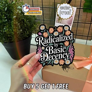 May include: A colorful sticker with the text "Radicalized by Basic Decency" surrounded by floral illustrations. The sticker is held in front of a gift box with a peach ribbon. Additional text reads "Buy 5 Get 1 Free".