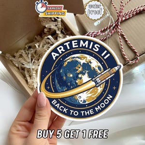 May include: A round sticker featuring the text "ARTEMIS II BACK TO THE MOON" with a graphic of a planet and a rocket. The sticker is blue, gold, and white. The image also includes a "water proof" sticker and a "SAMEDAY SHIPPING" sticker.