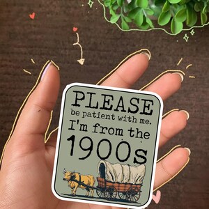 May include: A square sticker with the text "PLEASE be patient with me. I'm from the 1900s." features an illustration of a covered wagon pulled by a bull. The sticker has a green background and a white border.