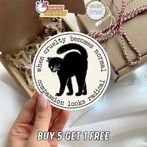 May include: A round sticker featuring a black cat silhouette with the text "when cruelty becomes normal, compassion looks radical." The sticker is cream-colored with black text and a black cat illustration. The sticker is waterproof.