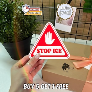 May include: A red and white triangular sticker with the words "STOP ICE" and a hand symbol. The sticker is held in front of a gift box with a peach ribbon. The text "BUY 5 GET 1 FREE" is at the bottom.