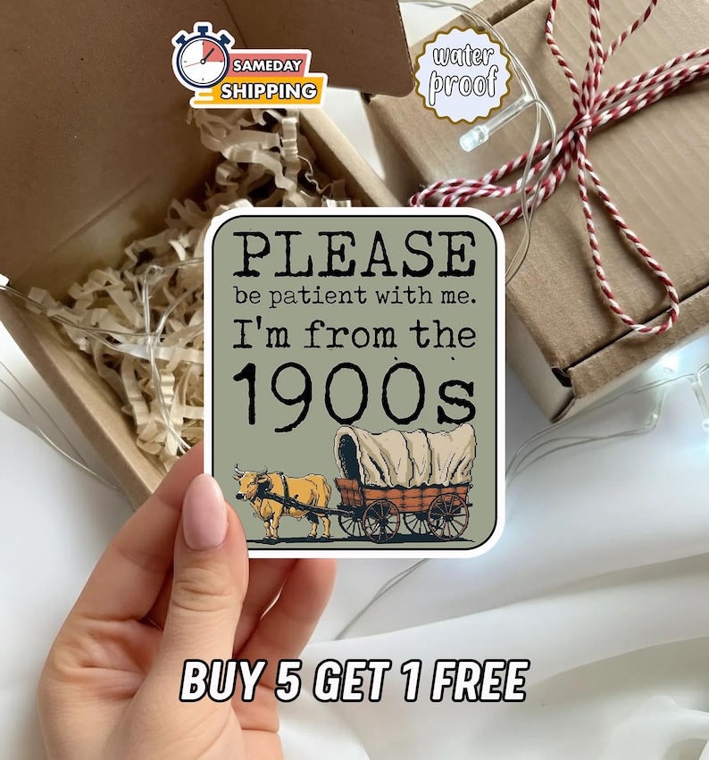 May include: A square sticker with the text "PLEASE be patient with me. I'm from the 1900s" and an illustration of a covered wagon pulled by a bull. The sticker is held in a hand, near a gift box.