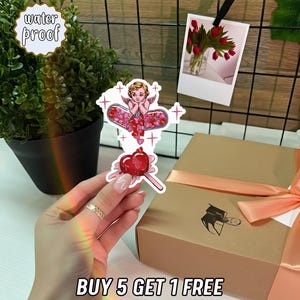 May include: A sticker set featuring a cherub with heart-shaped wings and a heart-shaped lollipop. The stickers are water-proof. A gift box with a peach ribbon and a photo of red tulips are in the background.