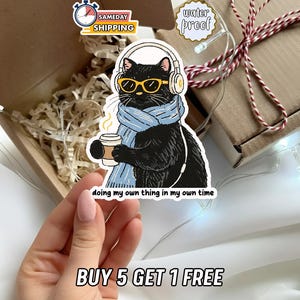 May include: A black cat sticker wearing headphones, yellow sunglasses, and a blue scarf, holding a coffee cup. The sticker has the text "doing my own thing in my own time" and "water proof". The sticker is in a box with a "Sameday Shipping" sticker.
