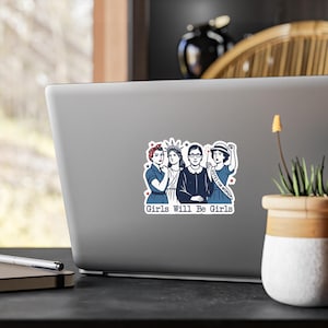 Pode incluir: Um autocolante com um gr&aacute;fico de quatro mulheres, incluindo a Est&aacute;tua da Liberdade e Ruth Bader Ginsburg, com o texto "Girls Will Be Girls". O design &eacute; em azul, branco e vermelho.