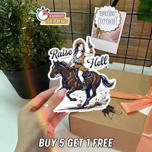 May include: A sticker featuring a cowgirl riding a horse, with the words "Raise Hell" in a stylized font. The cowgirl is holding a gun. The sticker also has a "water proof" and "sameday shipping" label.