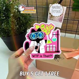 May include: A die-cut sticker featuring a black cat wearing blue goggles and a white lab coat, holding a test tube. The design includes neon green ghost shapes, laboratory glassware with colorful liquids, and the text "WTF is That?!" in pink.
