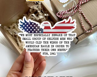 Könnte beinhalten: Ein Aufkleber mit einem Adler im Design der amerikanischen Flagge und dem Zitat: "WIR MÜSSEN UNS BESONDERS VOR DIESER KLEINEN GRUPPE SELBSTSÜCHTIGER MÄNNER HÜTEN, DIE DIE FLÜGEL DES AMERIKANISCHEN ADLERS STUTZEN WÜRDEN, UM IHRE EIGENEN NESTER ZU FEDERN." -FDR, 1941.