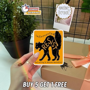 May include: A square sticker with an orange background features a black cat silhouette with the word "RESIST" inside. The text "introverted" and "but willing to discuss revolution" are above and below the cat. The sticker is labeled "water proof".