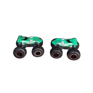 May include: Two green monster trucks with black tires and silver engine details are displayed. The trucks have a sleek design and are positioned side-by-side against a white background. The tires are large and rugged.