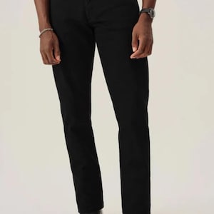 May include: Black denim jeans with a straight-leg cut. The jeans are worn with a silver buckle belt and black leather shoes. The model is wearing a white t-shirt and a silver bracelet. The trousers are approximately 102 cm in length.