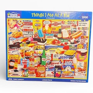 May include: A 1000-piece jigsaw puzzle titled "Things I Ate As A Kid" by White Mountain. The puzzle features a collage of vintage food products, including snacks, candies, and drinks, with a blue border and the text "USA Finest Quality."