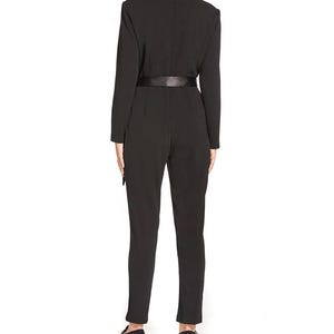 May include: A black jumpsuit with a satin belt and long sleeves. The jumpsuit has a mock neck and a fitted silhouette.