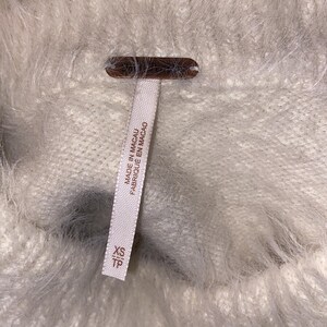 May include: White fuzzy sweater with a tag that reads "Made in Macau Fabrique en Macao" and "XS TP".